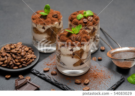 Classic tiramisu dessert in a glass on stone serving board on dark concrete background Classic tiramisu dessert in a glass on stone serving board on dark concrete background 54083029