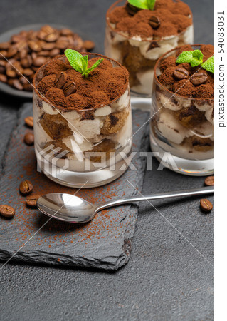 Classic tiramisu dessert in a glass on stone serving board on dark concrete background 54083031