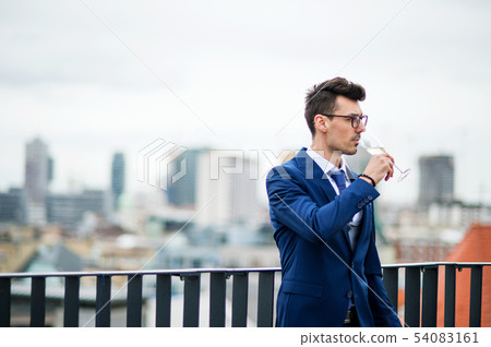 A young businessman with glass on a party outdoors on roof terrace in city. 54083161