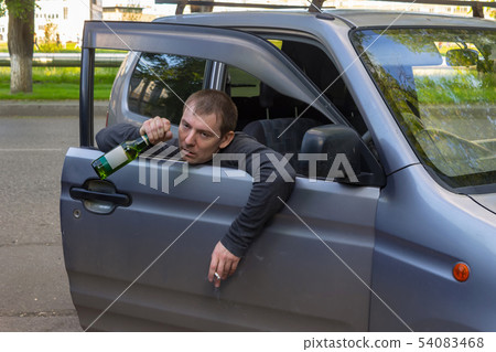 Drunk car driver with a bottle of beer in hand Drunk car driver with a bottle of beer in hand 54083468