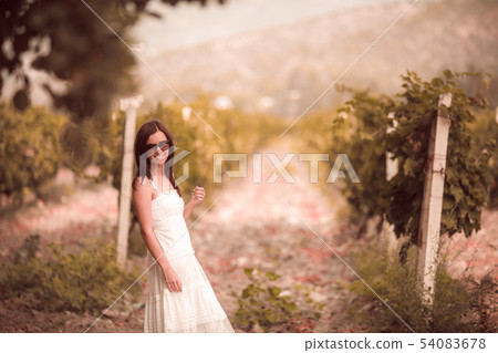 Smiling woman in white dress standing in vineyard 54083678