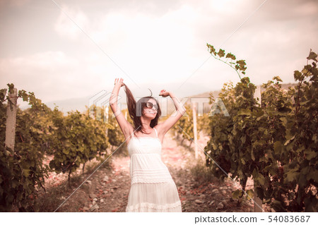 Smiling woman in white dress standing in vineyard Smiling woman in white dress standing in vineyard 54083687