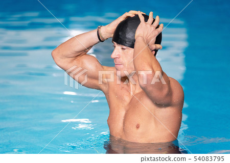 Young muscular swimmer preparing to swim, putting his cap on. Young muscular swimmer preparing to swim, putting his cap on. 54083795