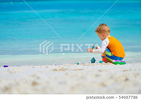 Three year old toddler playing on beach Three year old toddler playing on beach 54087786