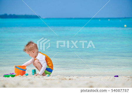 Three year old toddler playing on beach Three year old toddler playing on beach 54087787