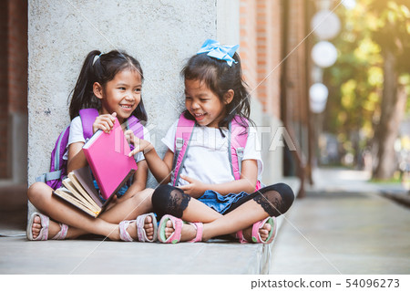 Two asian pupil girls reading a book together Two asian pupil girls reading a book together 54096273