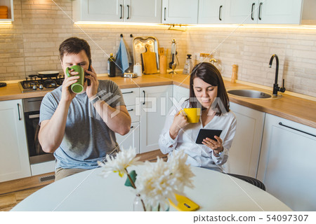couple sitting at the kitchen in the morning drinking tea reading news couple sitting at the kitchen in the morning drinking tea reading news 54097307