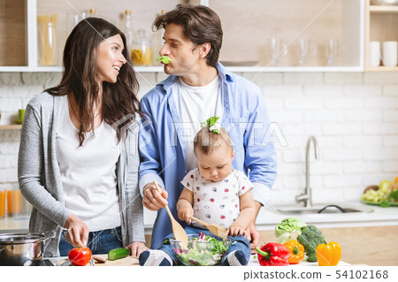 Photo of young loving couple parents with their little baby son cooking in kitchen. 54102168