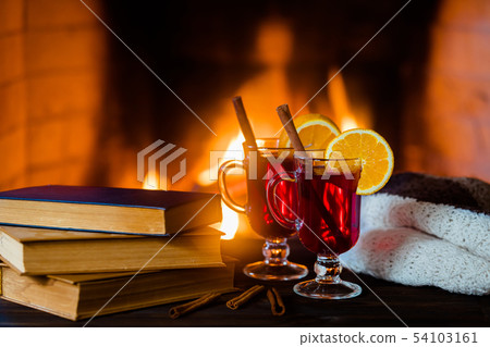 Hot mulled wine and a book on the table. Fireplace with fire on the background. 54103161