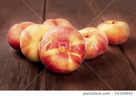 A closeup photo of vibrant organic flat saturn peaches on a dark rustic wooden background A closeup photo of vibrant organic flat saturn peaches on a dark rustic wooden background 54104945