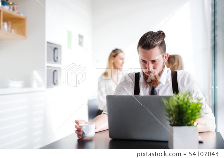 A portrait of young businessman with computer in an office, working. 54107043