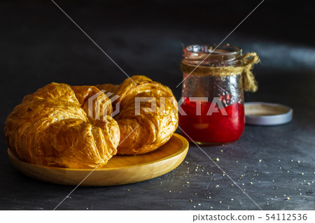 Croissant on wooden dish and strawberry jam bottle Croissant on wooden dish and strawberry jam bottle 54112536