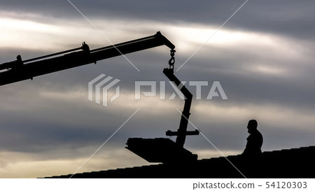 Silhouette of a crane and man on roof of home 54120303