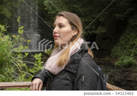 Young woman in front of a waterfall in Ireland 54121402