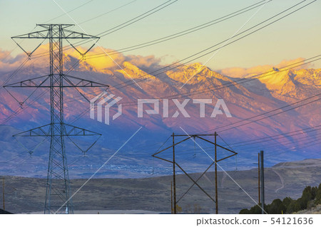 Powerlines silhouetted agains a mountain at sunet 54121636