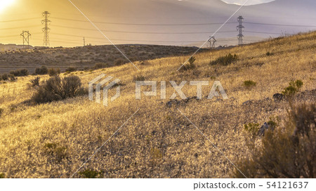 Power lines on grassy hills lit by bright sunlight 54121637