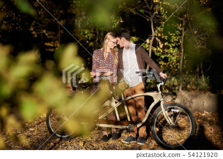 Romantic couple, man and attractive girl close together at tandem bicycle in dark autumn park. Romantic couple, man and attractive girl close together at tandem bicycle in dark autumn park. 54121920