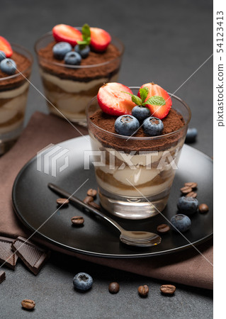 Classic tiramisu dessert with blueberries and strawberries in a glass on stone serving board on dark Classic tiramisu dessert with blueberries and strawberries in a glass on stone serving board on dark 54123413