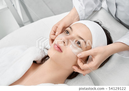 Brunette lying with patches under eyes in spa salon Brunette lying with patches under eyes in spa salon 54129122