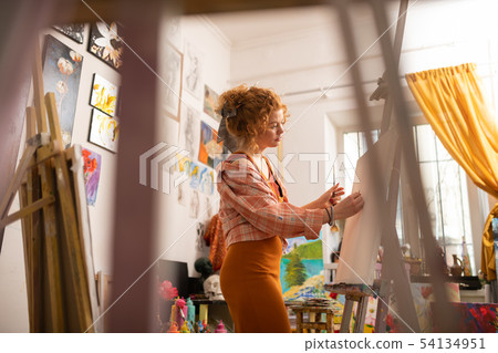 Artist wearing squared shirt painting on canvas in workshop 54134951