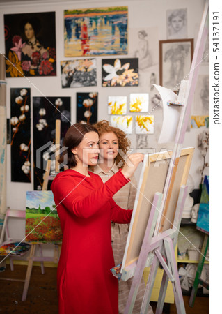 Artist painting on canvas standing near her friend Artist painting on canvas standing near her friend 54137191