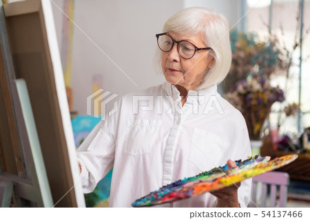 Talented retired woman painting standing near canvas 54137466