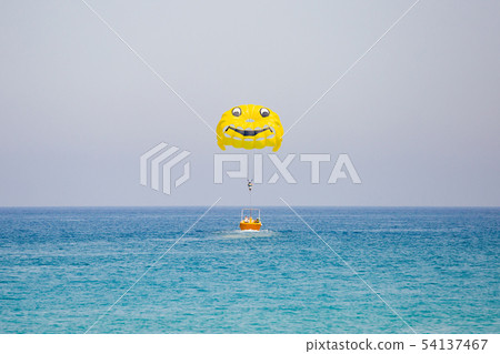 Woman flying on a yellow parachute with smiling face on it 54137467