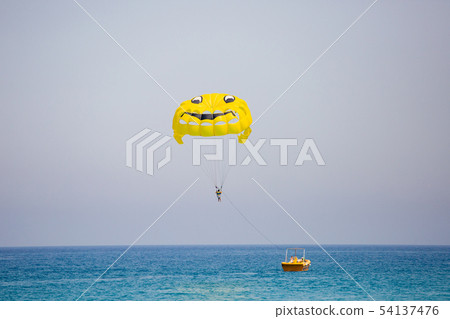 Woman flying on a yellow parachute with smiling face on it Woman flying on a yellow parachute with smiling face on it 54137476