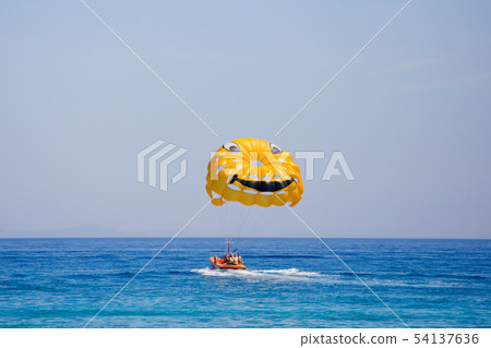 Couple of tourists flying on a yellow parachute with smiling face on it 54137636