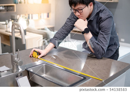 Asian man using tape measure on kitchen counter Asian man using tape measure on kitchen counter 54138583
