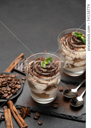 Classic tiramisu dessert in a glass on stone serving board on dark concrete background Classic tiramisu dessert in a glass on stone serving board on dark concrete background 54138774