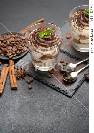 Classic tiramisu dessert in a glass on stone serving board on dark concrete background Classic tiramisu dessert in a glass on stone serving board on dark concrete background 54138776