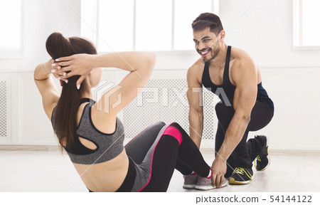 Young fit trainer helping girl doing sit ups in studio 54144122