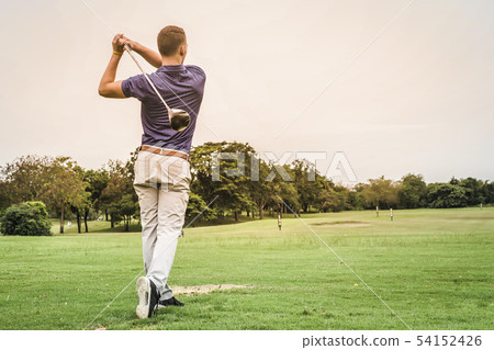 Back of golfer hitting ball on green field with Back of golfer hitting ball on green field with 54152426