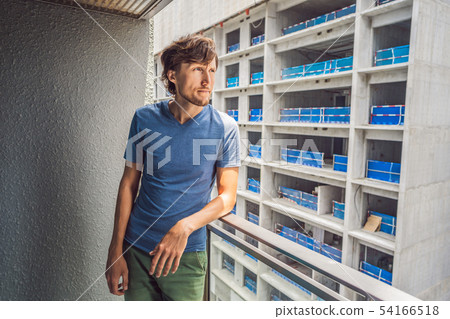 Young man on the balcony annoyed by the building works outside. Noise concept. Air pollution from Young man on the balcony annoyed by the building works outside. Noise concept. Air pollution from 54166518