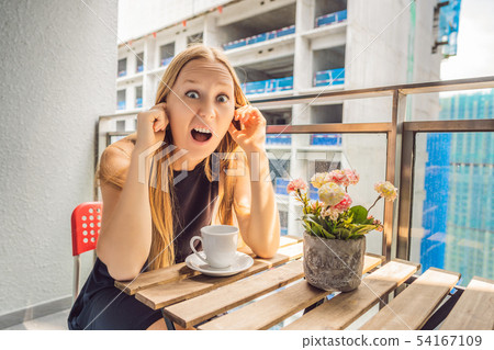 Young woman on the balcony annoyed by the building works outside. Noise concept. Air pollution from Young woman on the balcony annoyed by the building works outside. Noise concept. Air pollution from 54167109