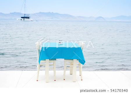 Cafe table served with a blue tablecloth near the sea coast for relaxing holidays vacations Cafe table served with a blue tablecloth near the sea coast for relaxing holidays vacations 54170340