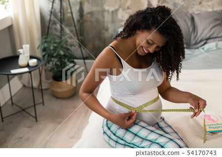 Expectant mother measuring her belly in bedroom. 54170743