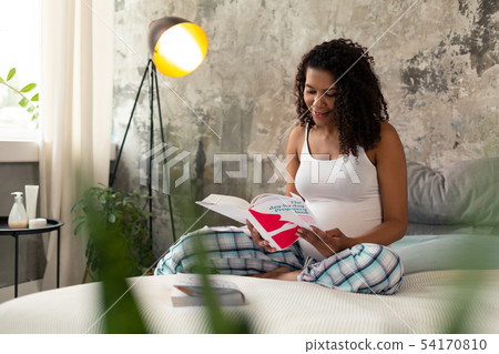 Pregnant woman sitting on her bed with a book. 54170810