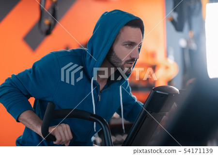 Dark-haired athletic man feeling thoughtful while cycling in gym 54171139