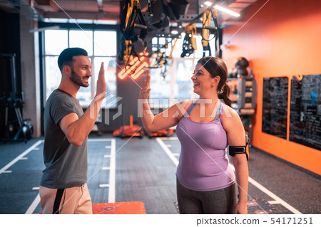 Dark-haired plump woman giving high five to her fitness trainer Dark-haired plump woman giving high five to her fitness trainer 54171251