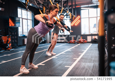 Dark-haired woman feeling exhausted while exercising on TRX Dark-haired woman feeling exhausted while exercising on TRX 54171995