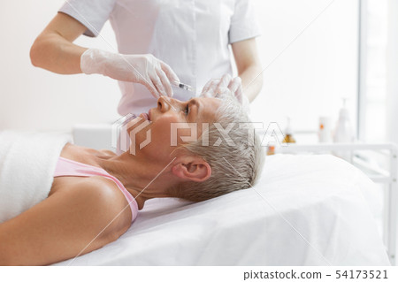 Nice grey haired woman receiving a forehead botox injection Nice grey haired woman receiving a forehead botox injection 54173521