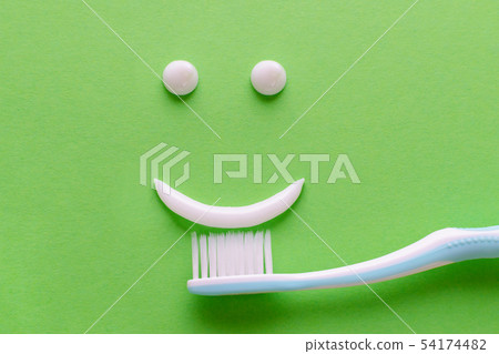 a face with smile from white toothpaste, teeth care concept, toothbrush on green background 54174482