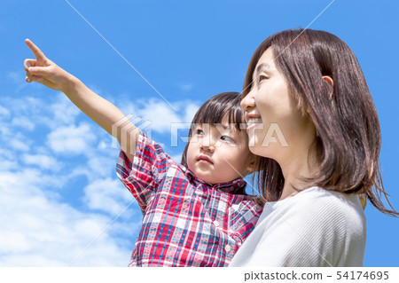 A little girl holding a mother against the blue sky and pointing to the upper left. A little girl holding a mother against the blue sky and pointing to the upper left. 54174695
