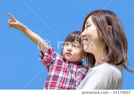 A little girl holding a mother against the blue sky and pointing to the upper left. A little girl holding a mother against the blue sky and pointing to the upper left. 54174697
