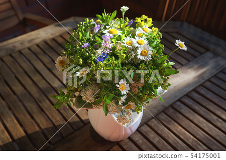 Bouquet of wild flowers in white vase on wooden table. 54175001