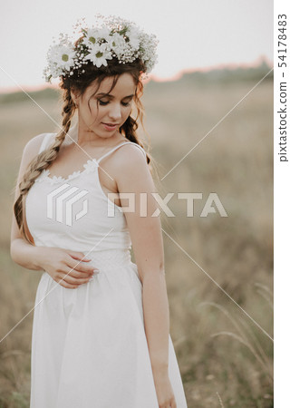 girl with braids and a floral wreath in a white boho dress in summer outdoors 54178483