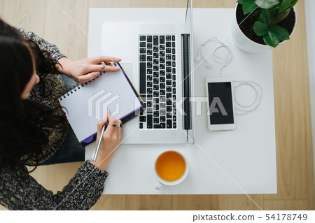 Businesswoman in front of laptop writing into the notepad. 54178749
