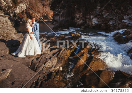 Amazing wedding couple, bride and groom holding hands on a mountains and rivers background. Cute 54178853